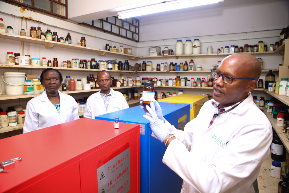 Mr. Mwaiwa Kivunzya, a Principal Investigator and Senior Technician (Right) showcasing one of the expensive chemical substances. Also present are Dr. Peter Dangili, a Senior Lecturer and Ms. Hellen Nchore, a Senior Technician (Left) at the chemistry storage lab.